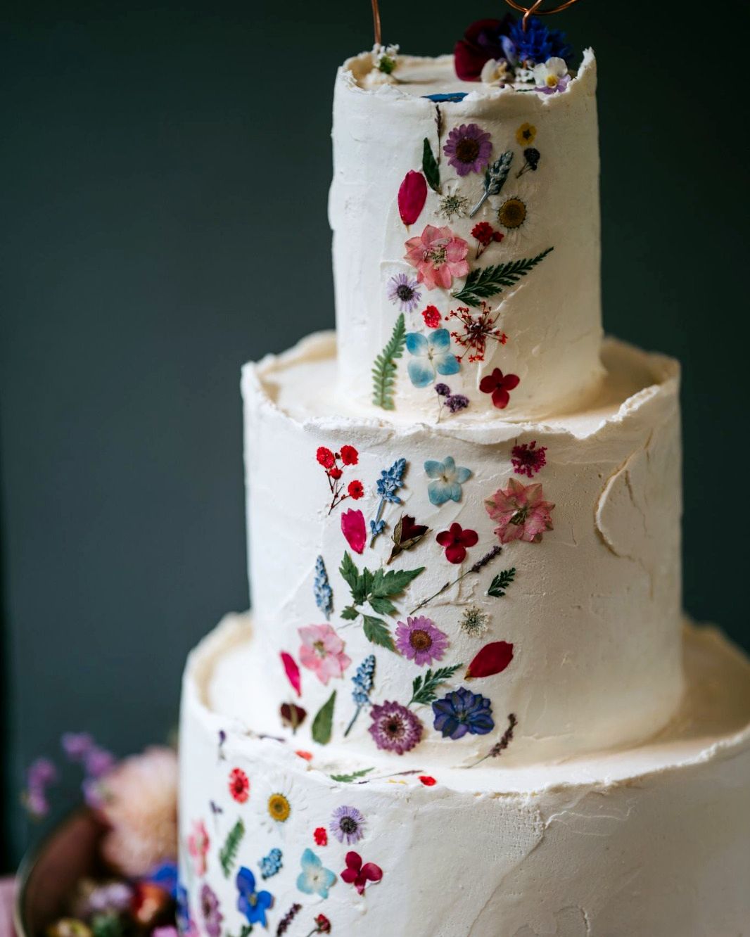 Three-tier white wedding cake decorated with pressed wildflowers