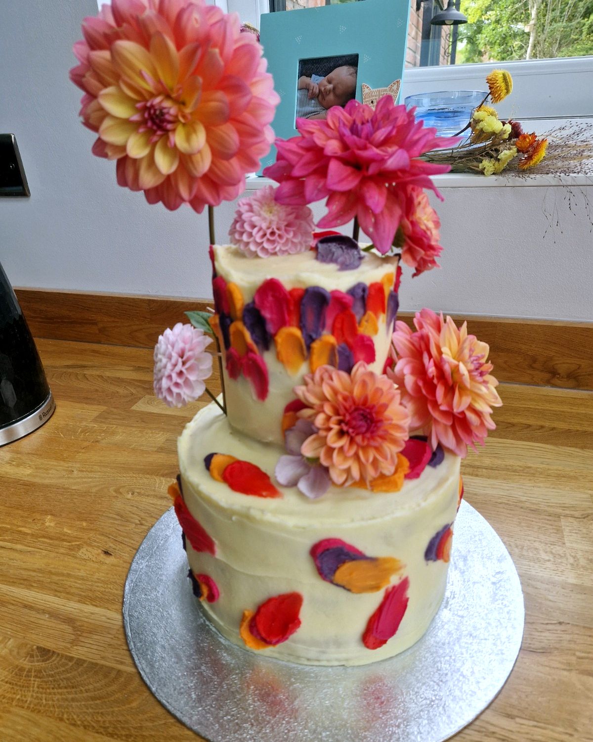 Two-tier cream cake with painted petals and orange and pink dahlias