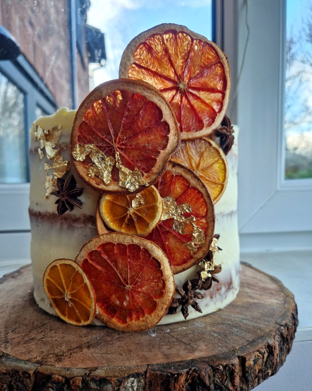 Semi-naked cake decorated with dried orange slices, star anise and gold leaf on a log slice