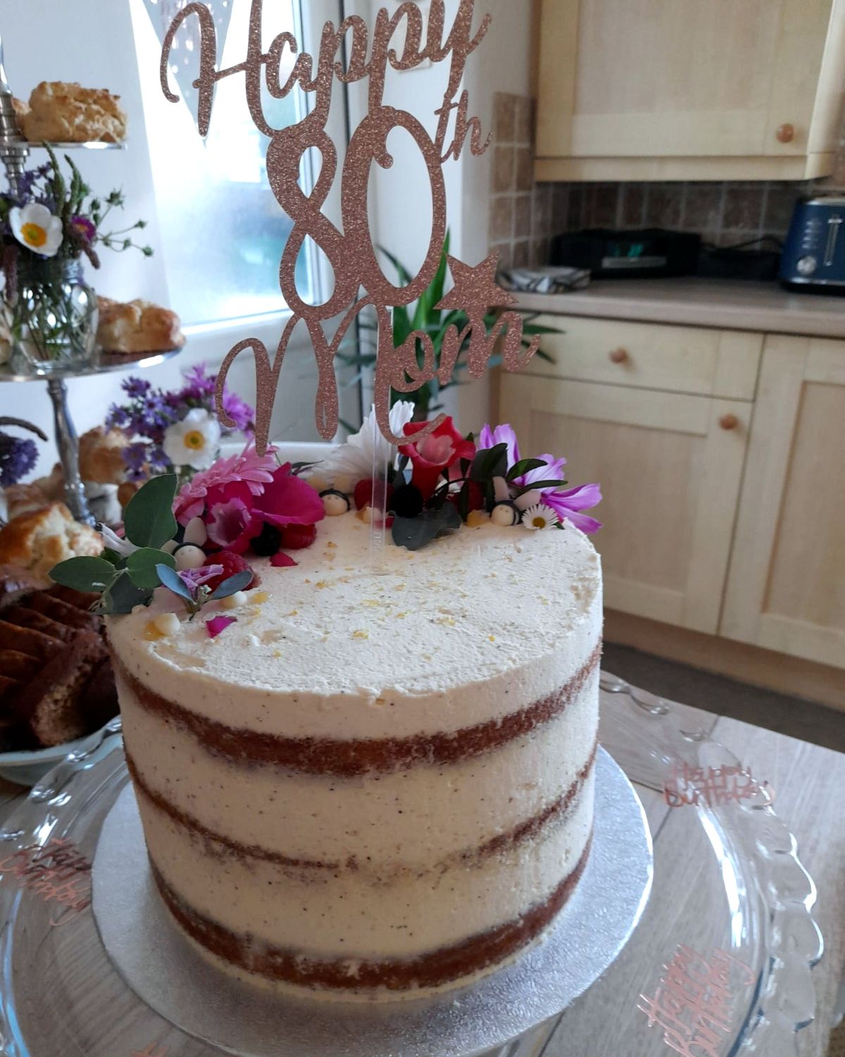 Semi-naked celebration cake with fresh flowers and a Happy 80th topper