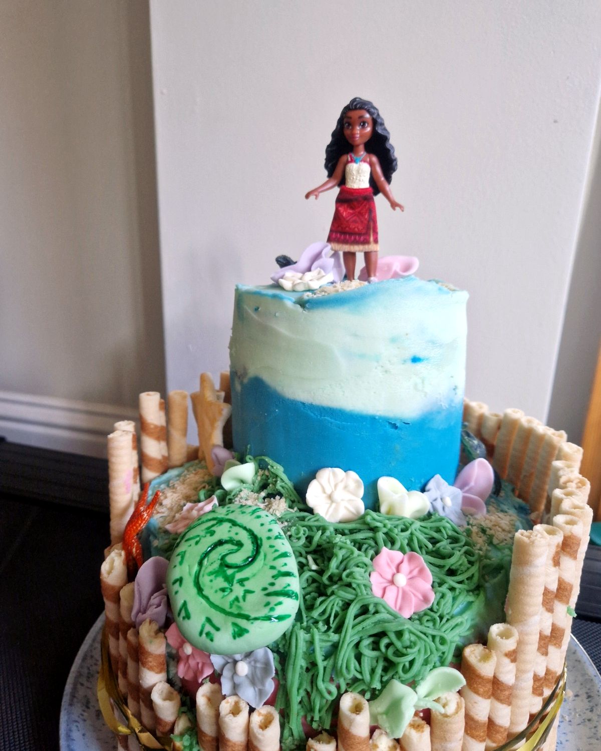Two-tier Moana-themed birthday cake with an ocean top tier and a doll